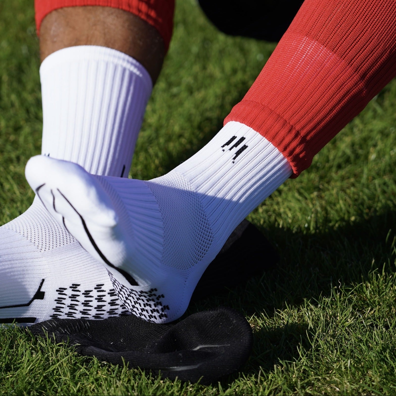 Joueur de foot avec des chaussettes antidérapantes blanches, chaussettes coupées et petits protèges tibias